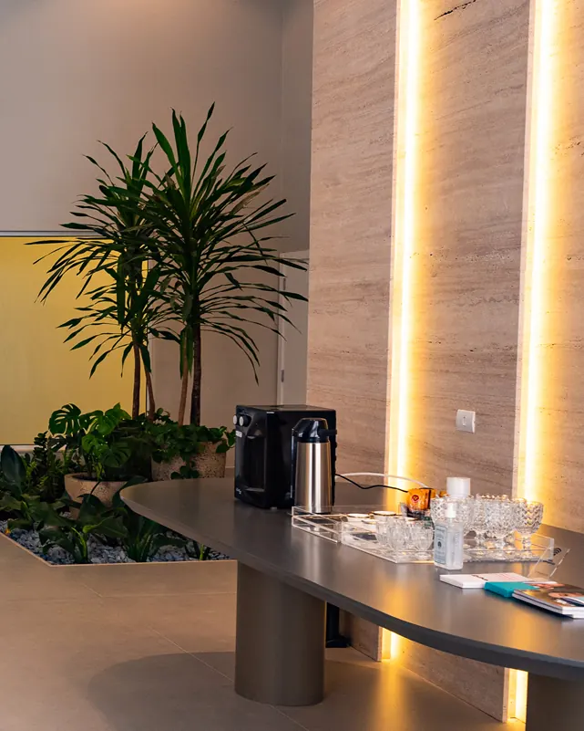 Recepção da Clínica Synergie: jardim interno, painel de madeira iluminado e mesa com café